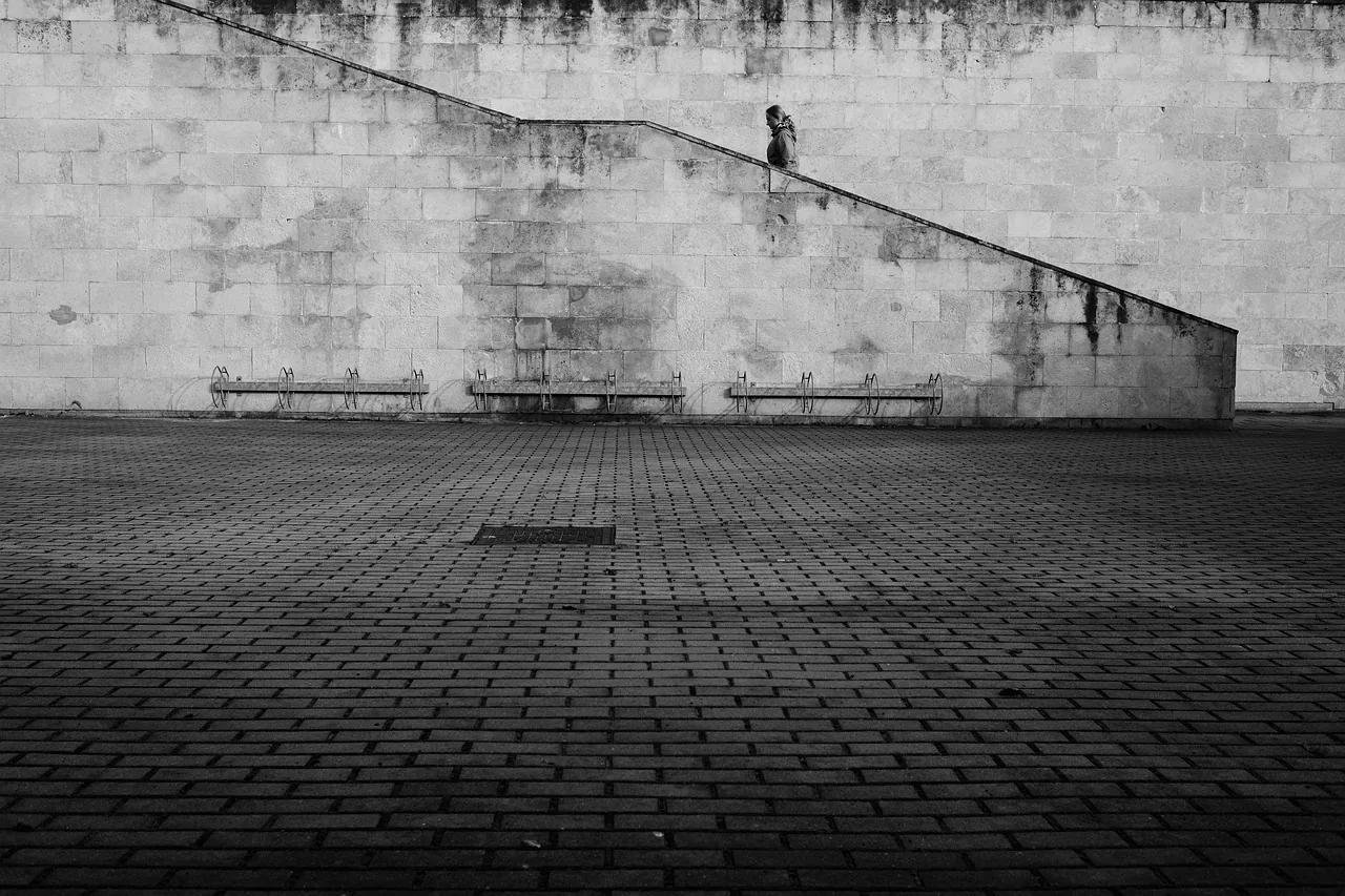 A figure climbing a long stone stair across a monumental wall