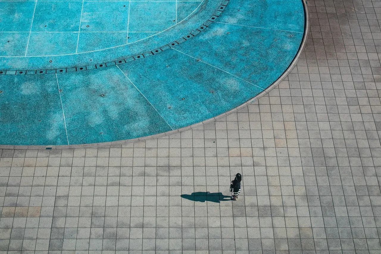 Aerial view of a turquoise courtyard pool, one figure casting a long shadow